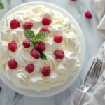 Fluffy 2-ingredient healthy cloud cake on a white cake stand, garnished with fresh raspberries and mint leaves, perfect for a light dessert.