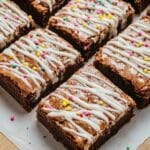 Close-up of freshly baked vanilla brownies with golden edges, drizzled with white chocolate glaze and garnished with sprinkles.