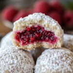 Raspberry-filled almond snowball cookies dusted with powdered sugar on a plate