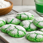 Bright green St. Patrick’s Day crinkle cookies coated in powdered sugar on a baking tray with a soft crackled texture.