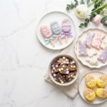 Assorted easy Easter desserts for kids displayed on white marble — egg cakesicles, bunny cookies, bark, and Rice Krispie treat eggs