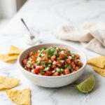 pico de gallo recipe in white bowl with tortilla chips on marble