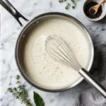 Saucepan of smooth bechamel sauce on marble
